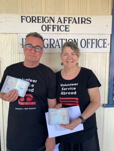 A couple smiling for the camera outside of the immigration office holding their passports