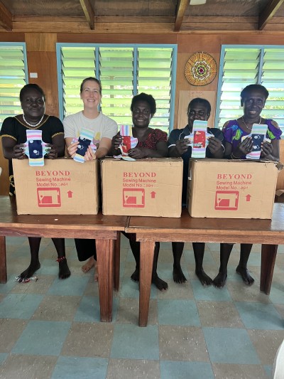 Women standing and smiling for the camera while holding the sanitary pads that they've just learnt to sew