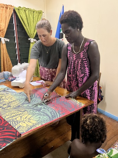 One woman cutting a piece of fabric while another woman guides her