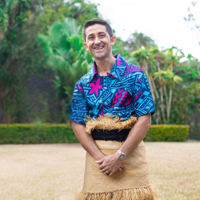 Man standing and smiling for the camera in front of a yard and palm trees
