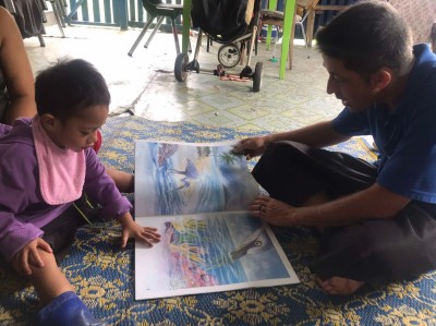 A man and child seated on the floor reading a picture book together